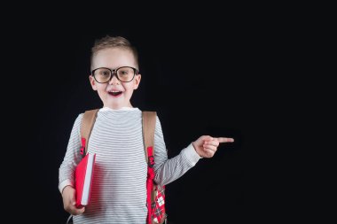 Siyah bir arka plan üzerinde neşeli gülümseyen küçük çocuk. Kameraya bakıyorum. Okul konsepti