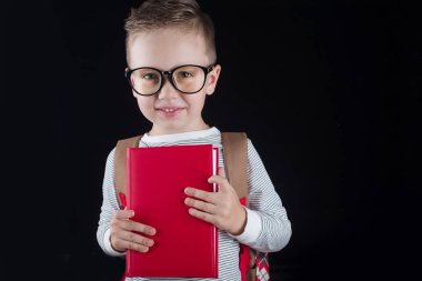 Siyah bir arka plan üzerinde neşeli gülümseyen küçük çocuk. Kameraya bakıyorum. Okul konsepti