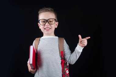 Siyah bir arka plan üzerinde neşeli gülümseyen küçük çocuk. Kameraya bakıyorum. Okul konsepti