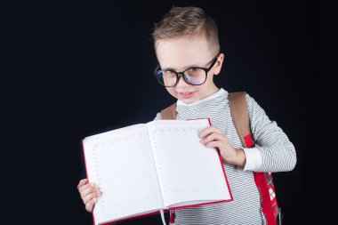 Siyah bir arka plan üzerinde neşeli gülümseyen küçük çocuk. Kameraya bakıyorum. Okul konsepti