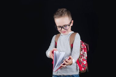 Siyah bir arka plan üzerinde neşeli gülümseyen küçük çocuk. Kameraya bakıyorum. Okul konsepti