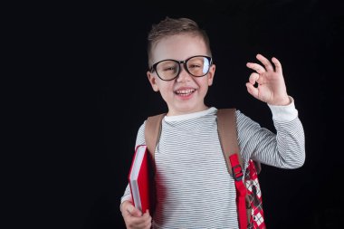 Siyah bir arka plan üzerinde neşeli gülümseyen küçük çocuk. Kameraya bakıyorum. Okul konsepti