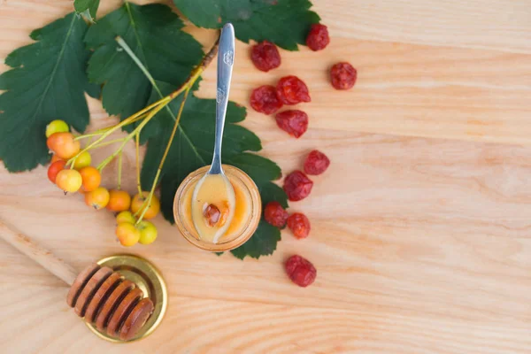 Schmackhafter und aromatischer Honig im Glas mit Vogelbeeren und Viburnum auf einem Holztisch. — Stockfoto