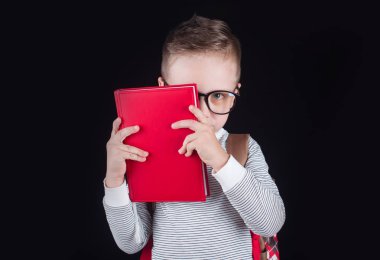 Siyah bir arka plan üzerinde neşeli gülümseyen küçük çocuk. Kameraya bakıyorum. Okul konsepti