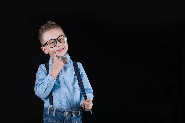 Fröhlich lächelnder kleiner Junge auf schwarzem Hintergrund. Blick in die Kamera. Schulkonzept — Stockfoto