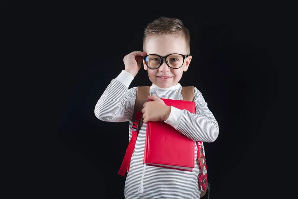 Fröhlich lächelnder kleiner Junge auf schwarzem Hintergrund. Blick in die Kamera. Schulkonzept — Stockfoto