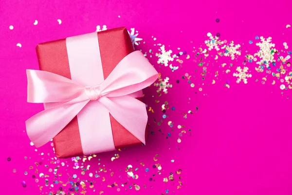 Caja de regalo roja con lazo rosa sobre fondo rosa con purpurina. Concepto de vacaciones . —  Fotos de Stock