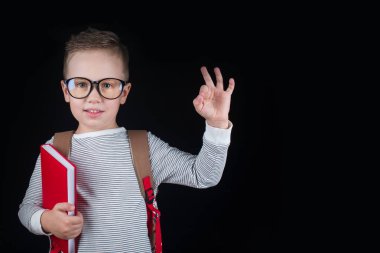 Siyah bir arka plan üzerinde neşeli gülümseyen küçük çocuk. Kameraya bakıyorum. Okul konsepti