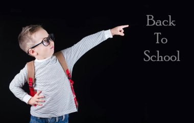 Siyah bir arka plan üzerinde neşeli gülümseyen küçük çocuk. Kameraya bakıyorum. Okul konsepti