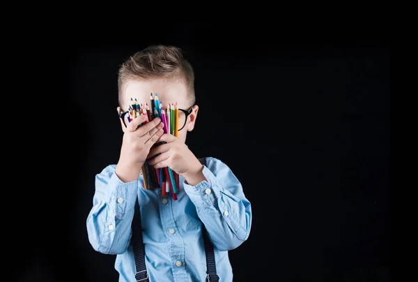 Fröhlich lächelnder kleiner Junge auf schwarzem Hintergrund. Blick in die Kamera. Schulkonzept — Stockfoto