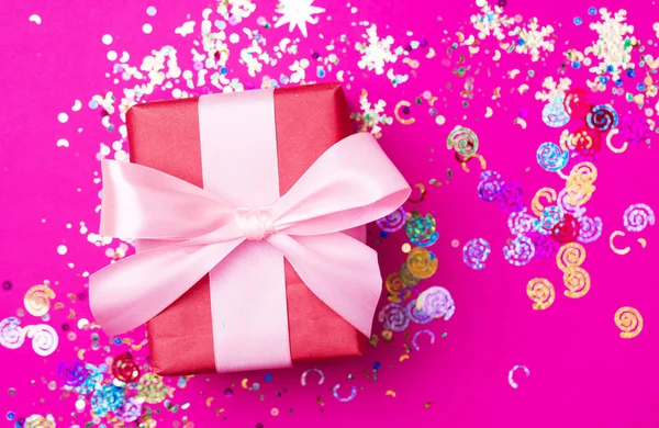 Caja de regalo roja con lazo rosa sobre fondo rosa con purpurina. Concepto de vacaciones . —  Fotos de Stock