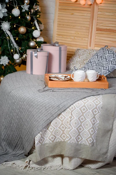 New Year\'s decor on a soft bed. Christmas tree with toys. Festive pink boxes.