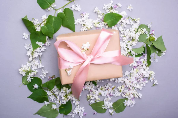 A beautiful gift with a satin ribbon against the background of lilac flowers. Mother\'s Day Holiday Content