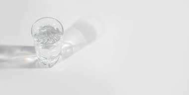 Arka planda parlak ışık ve yansıması olan temiz su dolu cam bardak. Metin için bir yer.