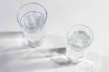 Arka planda parlak ışık ve yansıması olan temiz su dolu cam bardak. Metin için bir yer.