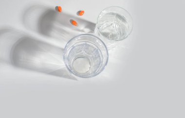 A glass of clean water with natural vitamins, with shadows on a light background. View from above. Healthcare clipart