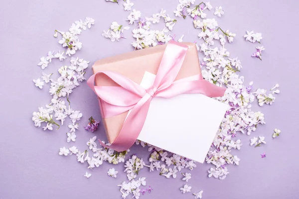 A beautiful gift with a satin ribbon against the background of lilac flowers. Mother\'s Day Holiday Content