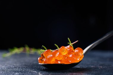 Siyah zemin üzerinde kaşık ve buz olan cam tabakta somon balığı havyarı..