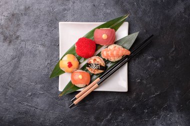 Pirinçten yapılmış suşi ruloları, füme yılan balığı, krem peynir ve uçan balık köftesi avacado, somon, krem peynir, yosun, soya sosu, karanlık bir masada zencefil. Suşi