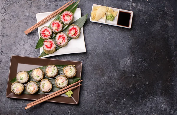 Set hot rolls with avacado, salmon, cream cheese, seaweed, soy sauce, ginger on a dark table. Sushi