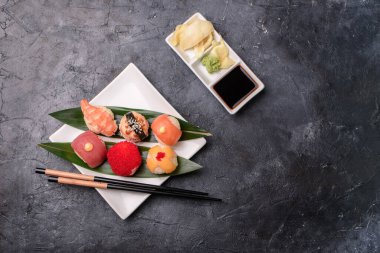 Pirinçten yapılmış suşi ruloları, füme yılan balığı, krem peynir ve uçan balık avacado, somon balığı, krem peynir, yosun, soya sosu, karanlık bir masada zencefil. Suşi