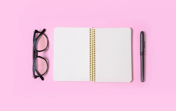 Notebook with clean sheets for records, hand holds pen, office glasses on a pink background. Flat lay. Office content