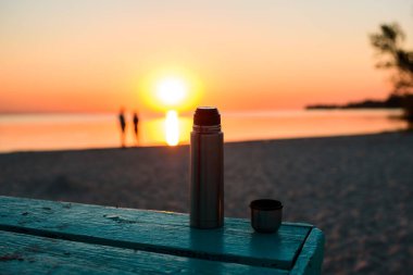 Sahilde güneşin doğuşu, kıyıya yakın aşık çift, bankta mis kokulu çay kokulu termos. Sabahın köründe deniz kenarında
