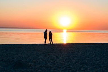 Sahilde güneşin doğuşu, kıyıya yakın aşık çift, bankta mis kokulu çay kokulu termos. Sabahın köründe deniz kenarında