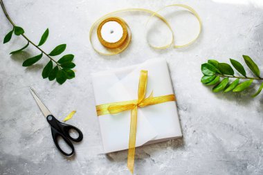 Güzel beyaz bir kağıtta hediye paketi, altın bir kurdele. Yeşil bitkiler, makaslar. El yapımı paketleme