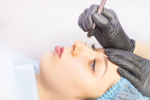 Permanent microblading tattooing freckles to a woman in a beauty salon