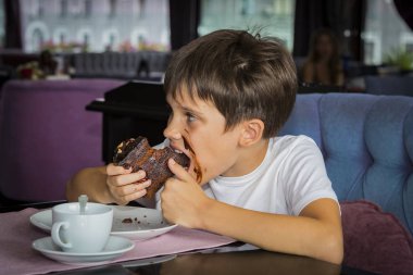 Oğlan elinde büyük bir dilim pasta yiyor 