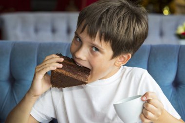 Oğlan elinde büyük bir dilim pasta yiyor 