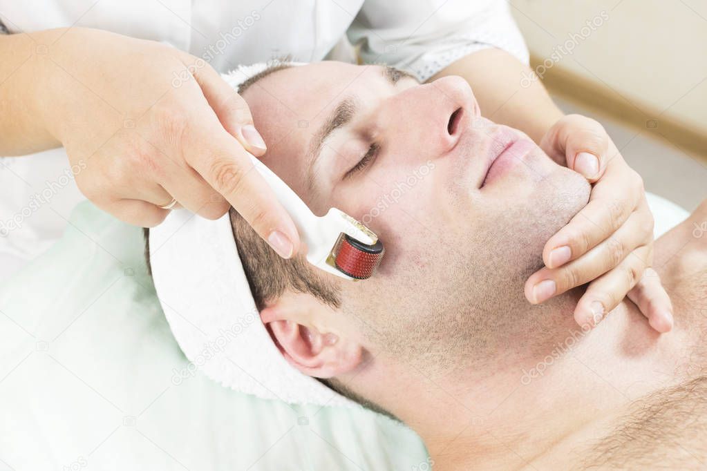 The man undergoes the procedure of medical micro needle therapy with a modern medical instrument derma roller.