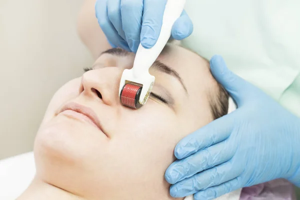 The woman undergoes the procedure of medical micro needle therapy with a modern medical instrument derma roller.
