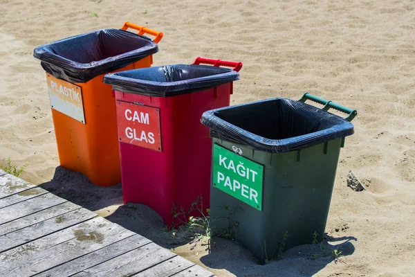 Three plastic trash cans for separate garbage on a sandy beach.