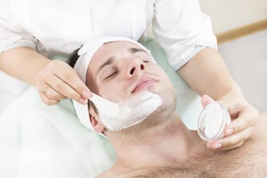 Bir güzellik salonunda genç bir adam için terapötik maske uygulamak için kozmetik prosedür.