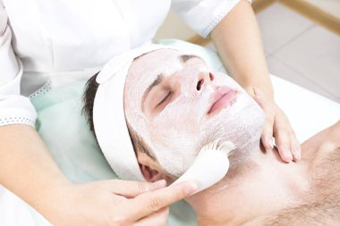 Bir güzellik salonunda genç bir adam için terapötik maske uygulamak için kozmetik prosedür.