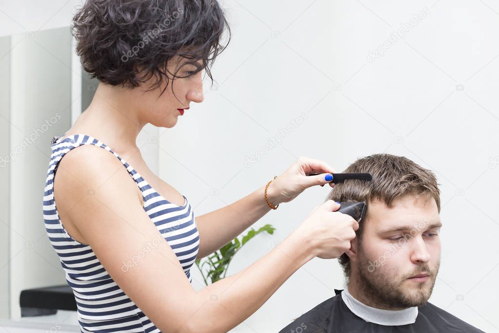 Woman haircuts a young guy in a hairdresser.