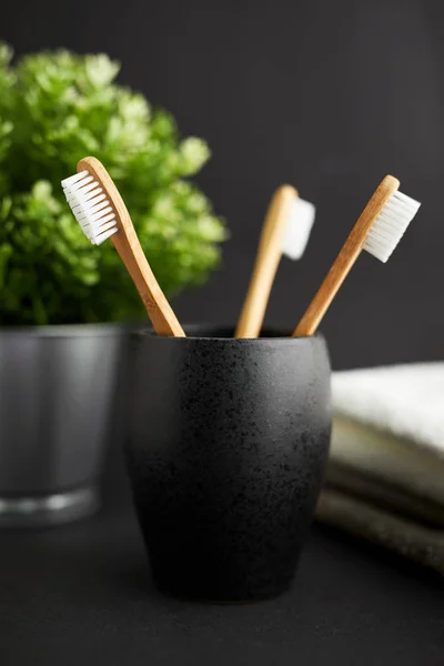 Three bamboo toothbrushes in a black glass with plant on a dark background — Stock Photo, Image