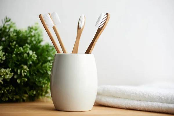 Four bamboo toothbrushes in a glass on a wooden background — Stock Photo, Image