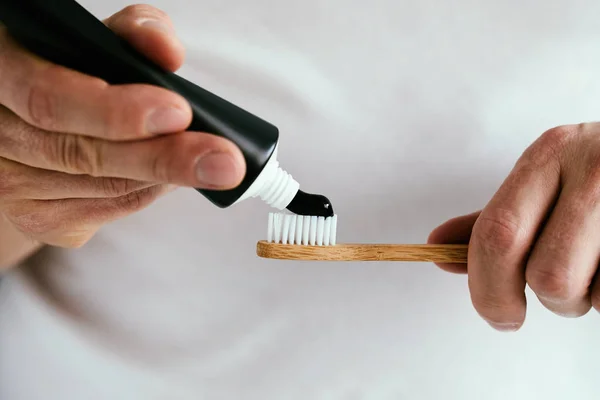 Male hands with a black toothpaste and a bamboo toothbrush — Stock Photo, Image