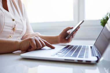 Kadın ofiste dizüstü bilgisayar ve cep telefonu ile çalışır