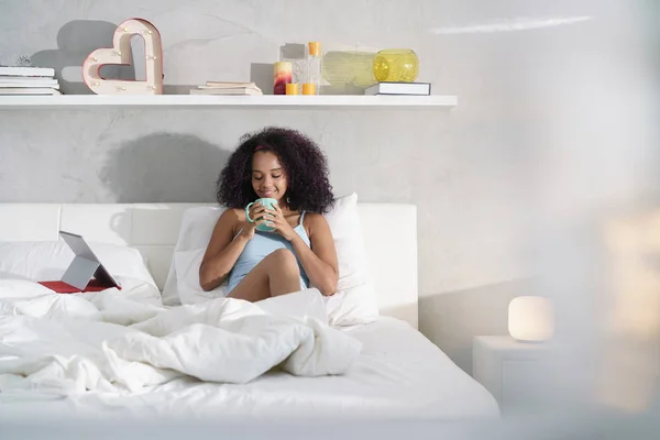 Frau trinkt am Sonntag Kaffee und schaut Film im Bett — Stockfoto