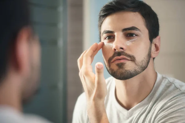 Hombre joven aplicando loción antienvejecimiento para el cuidado de la piel —  Fotos de Stock