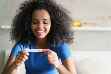Gebelik test kiti holding, sonuç için bekleyen mutlu genç latina kadın. Evde yatakta joy için gülümseyen euphoric İspanyol kız.