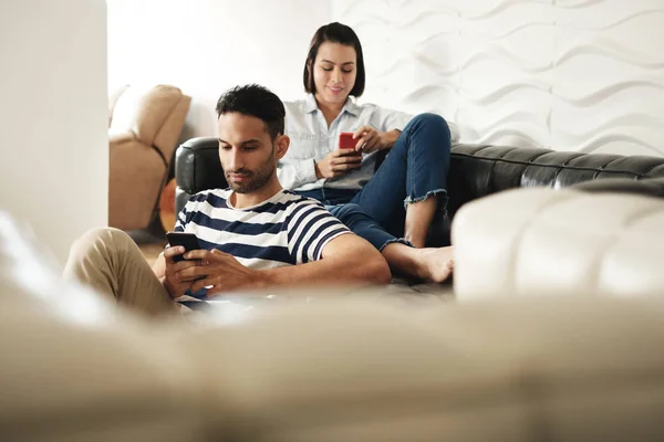 Pareja hispana feliz usando teléfonos inteligentes en el sofá en casa — Foto de Stock