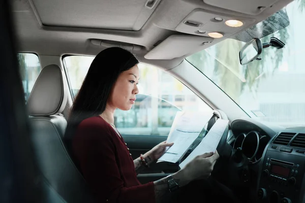 Занятая китайская деловая женщина, работающая в автомобиле с документами — стоковое фото