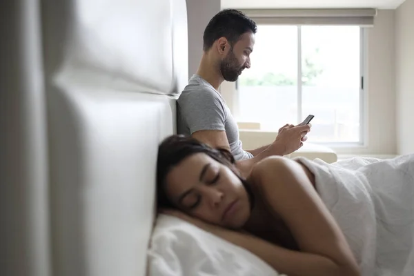 Pareja en la cama con el hombre infiel mensajes de texto en el teléfono inteligente — Foto de Stock