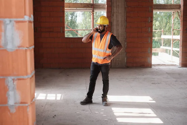 Hombre trabajando en el sitio de construcción sonriendo y usando Smartphone —  Fotos de Stock