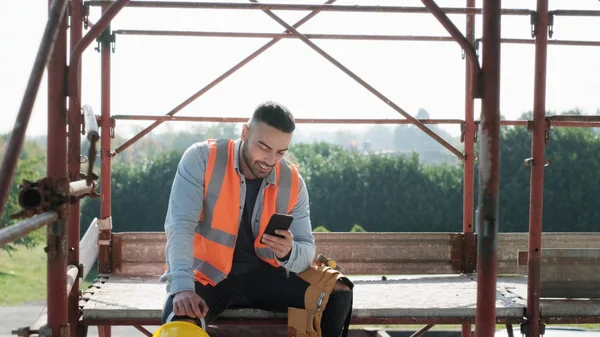 Mann, der auf Baustelle arbeitet, lächelt und nutzt Smartphone — Stockfoto